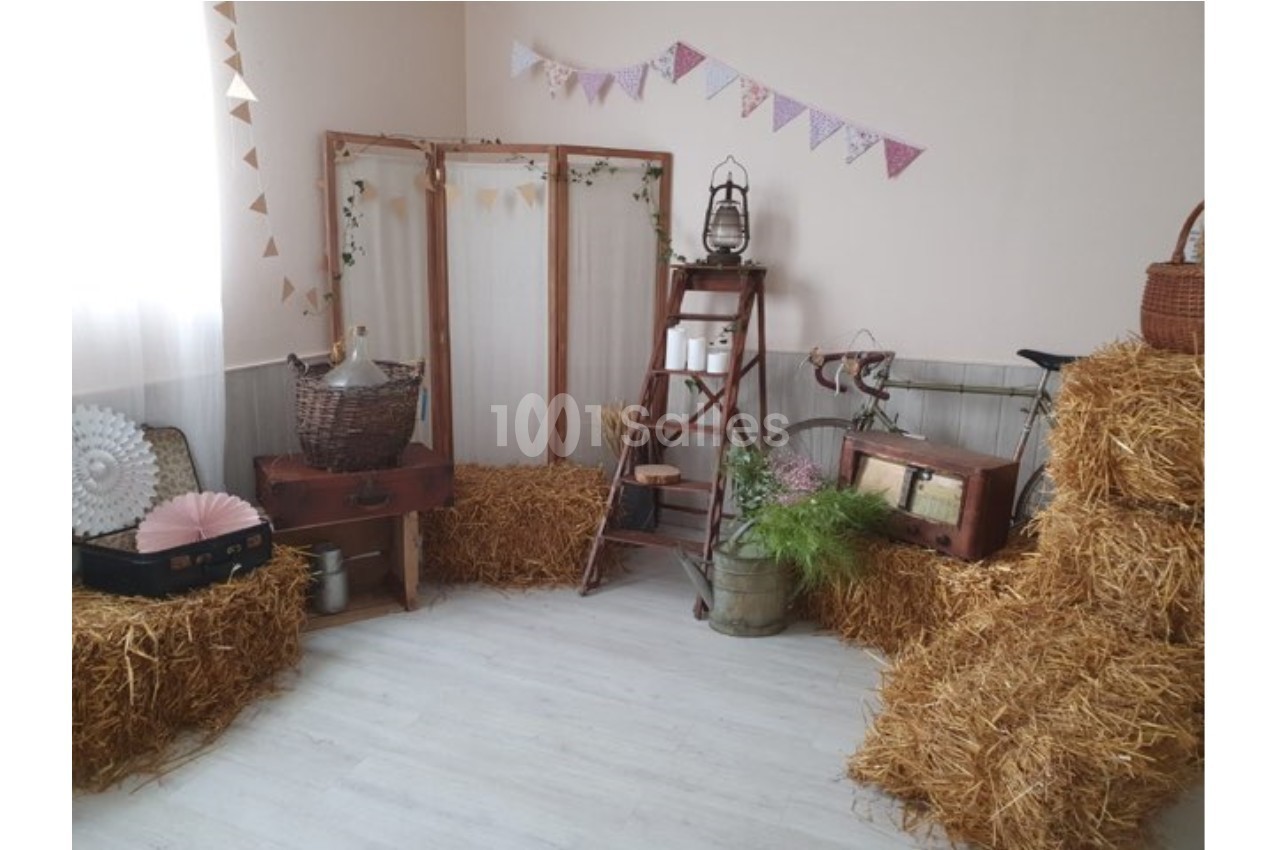 Décoration champêtre avec bottes de paille, échelle en bois, objets vintage et guirlandes dans une pièce lumineuse.