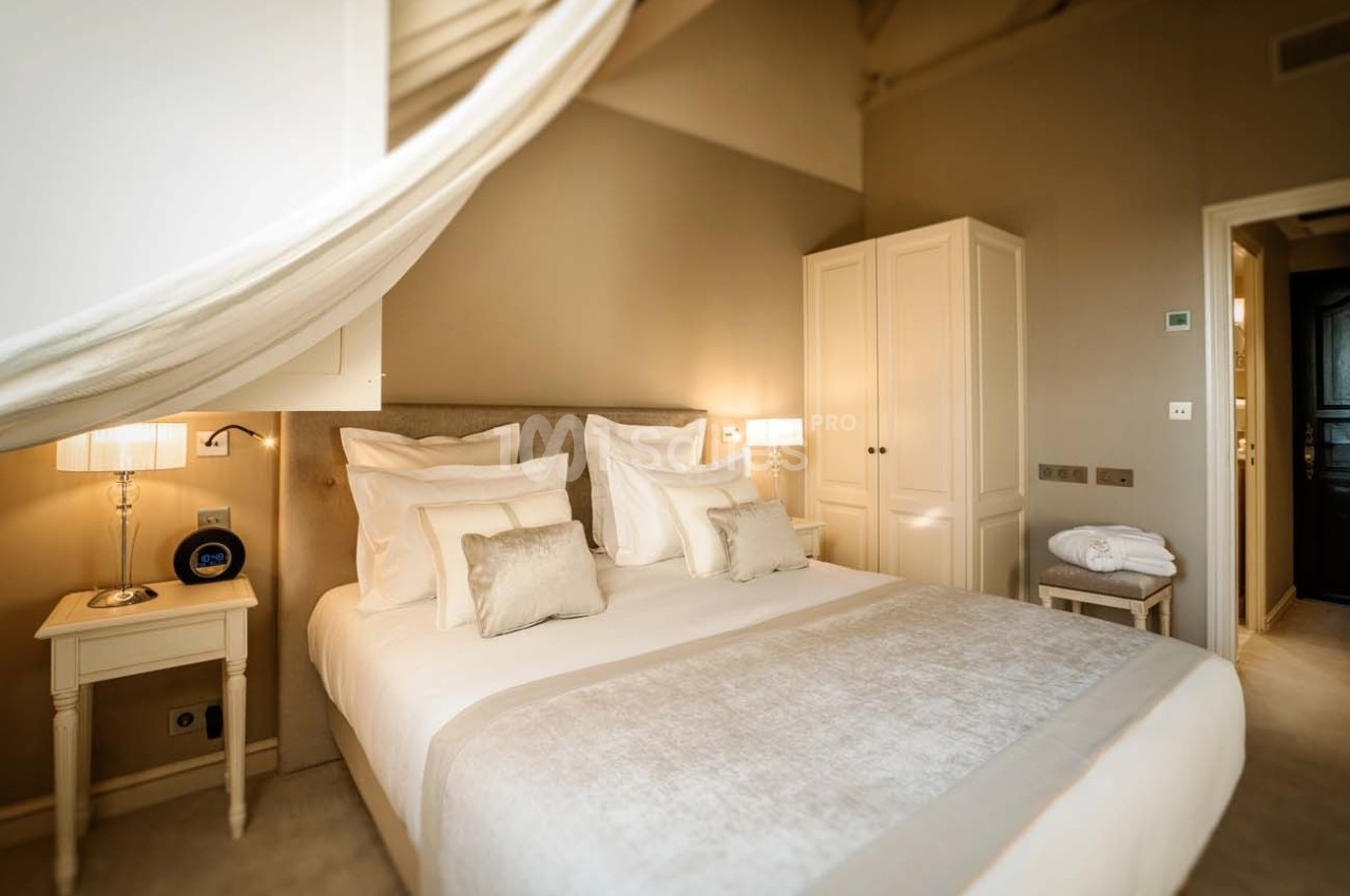 Chambre lumineuse avec lit double, draps blancs, tables de chevet, lampes et armoire dans un décor neutre et apaisant.