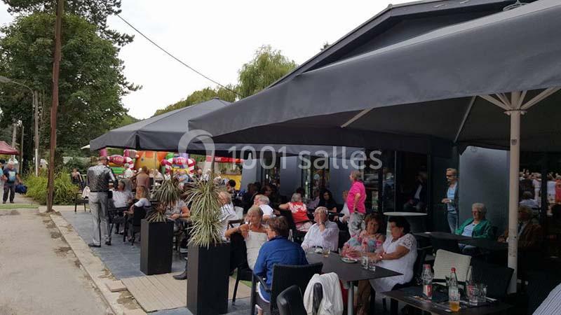 Terrasse d'un café animée avec des clients assis sous de grands parasols, entourée de verdure.