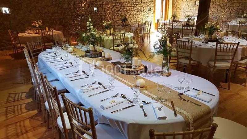 Salle de réception avec tables décorées de nappes blanches, bougies, fleurs et chaises en bois.