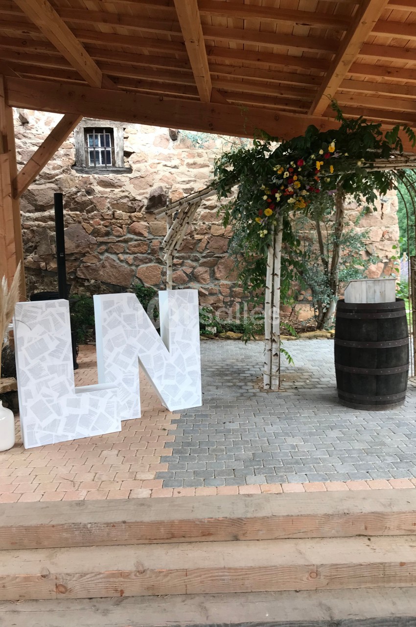 Structure en bois avec décorations de mariage, incluant des lettres blanches, un tonneau et des fleurs suspendues.