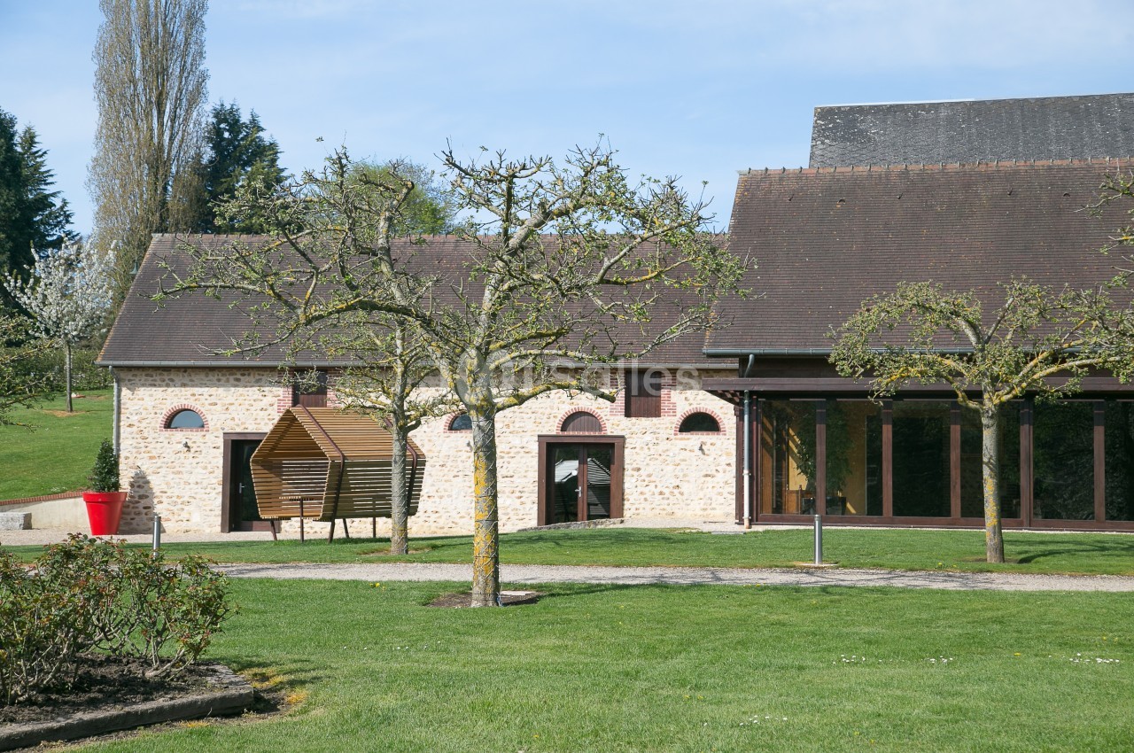 Bâtiment en pierre avec toit en ardoise, entouré d'arbres et d'une pelouse bien entretenue sous un ciel dégagé.