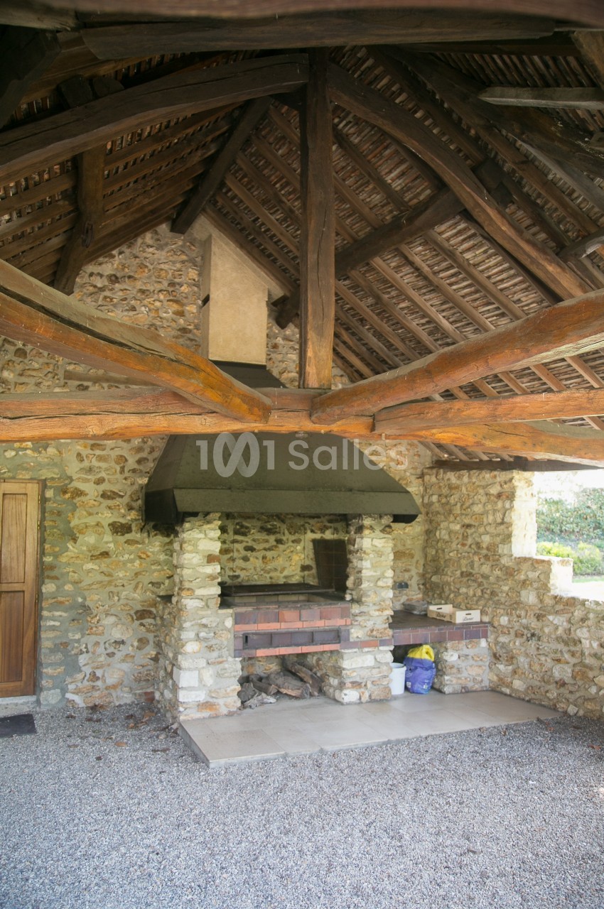 Abri en pierre avec toit en bois, abritant un barbecue en briques et des accessoires de jardinage.