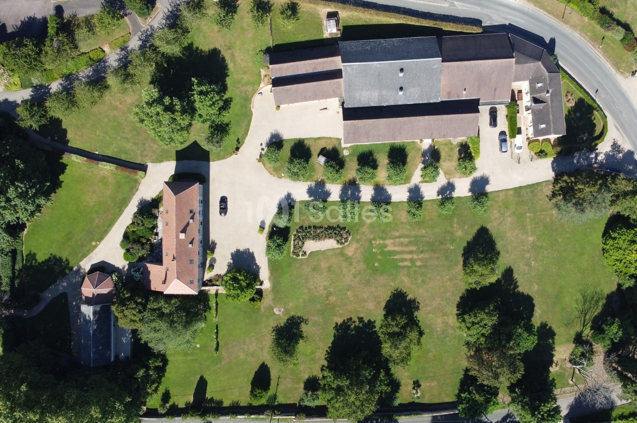 Vue aérienne d'un domaine avec bâtiments, allées, jardins et espaces verts entourés d'arbres.