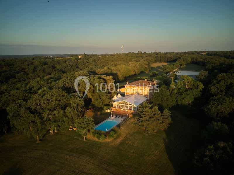 Vue aérienne d'un domaine entouré de forêt avec une grande maison, une piscine et une tente blanche dans un jardin.