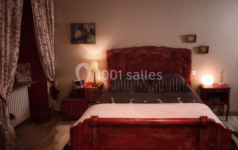 Chambre avec lit en bois sculpté, linge sombre, lampes allumées et décorations murales dans une ambiance chaleureuse.
