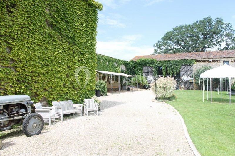 Cour extérieure avec murs couverts de lierre, mobilier de jardin, tracteur ancien et pelouse bordée d'arbres.