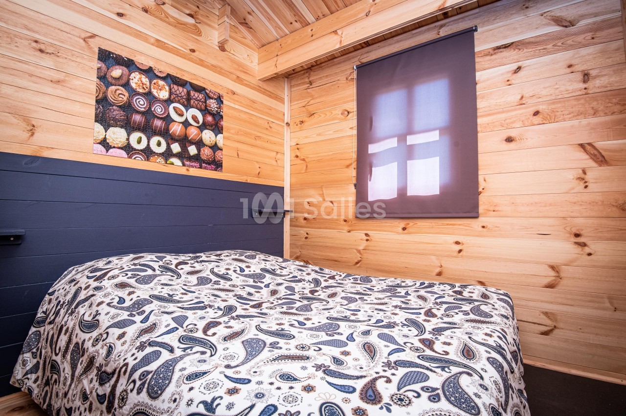 Chambre en bois avec un lit à motif paisley, un tableau mural coloré et une fenêtre avec un store occultant.