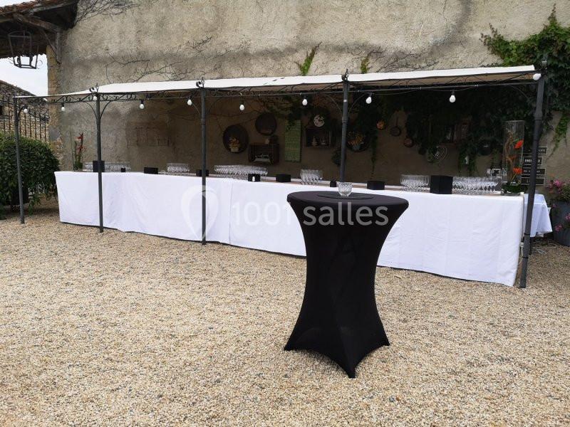 Table dressée pour un buffet en extérieur sous un auvent, avec une table haute noire au premier plan.