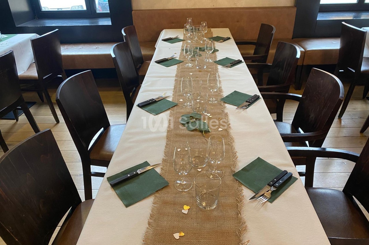 Table dressée avec nappe beige, chemin de table en toile de jute, serviettes vertes et couverts disposés.