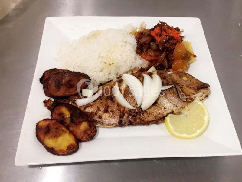 Assiette contenant du poisson grillé avec oignons, riz blanc, bananes plantains frites et légumes sautés.
