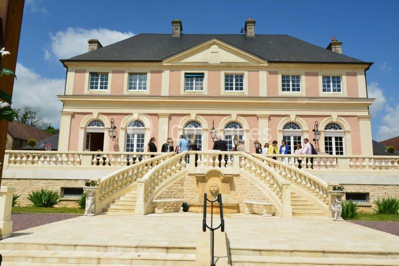 Façade d'un grand bâtiment classique avec escalier central, balustrades et personnes rassemblées sur la terrasse.