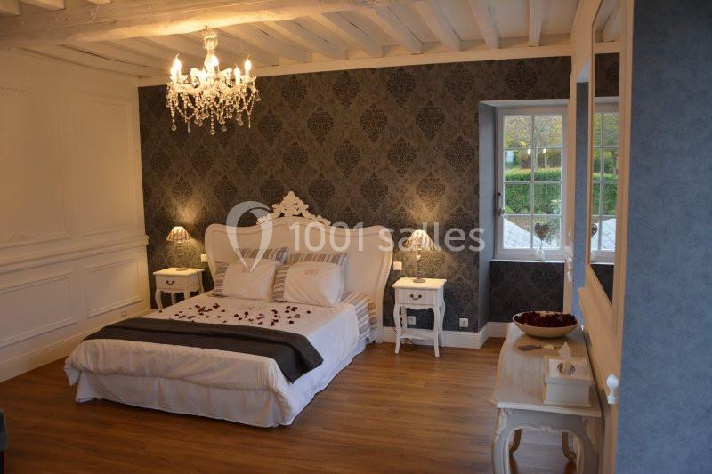 Chambre élégante avec lit double, lustre, murs décorés de papier peint sombre et vue sur un jardin par la fenêtre.