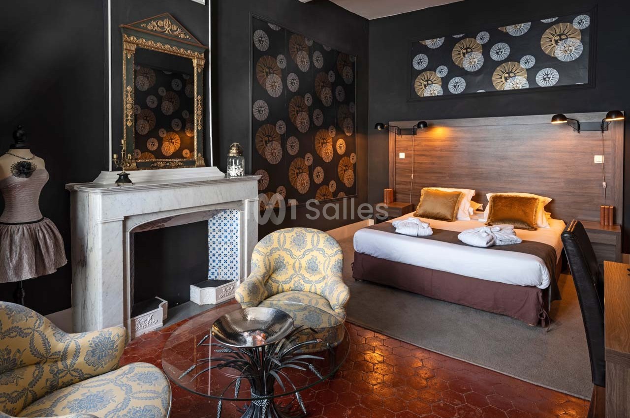 Chambre élégante avec lit double, cheminée décorative, fauteuils jaunes et murs ornés de motifs floraux.