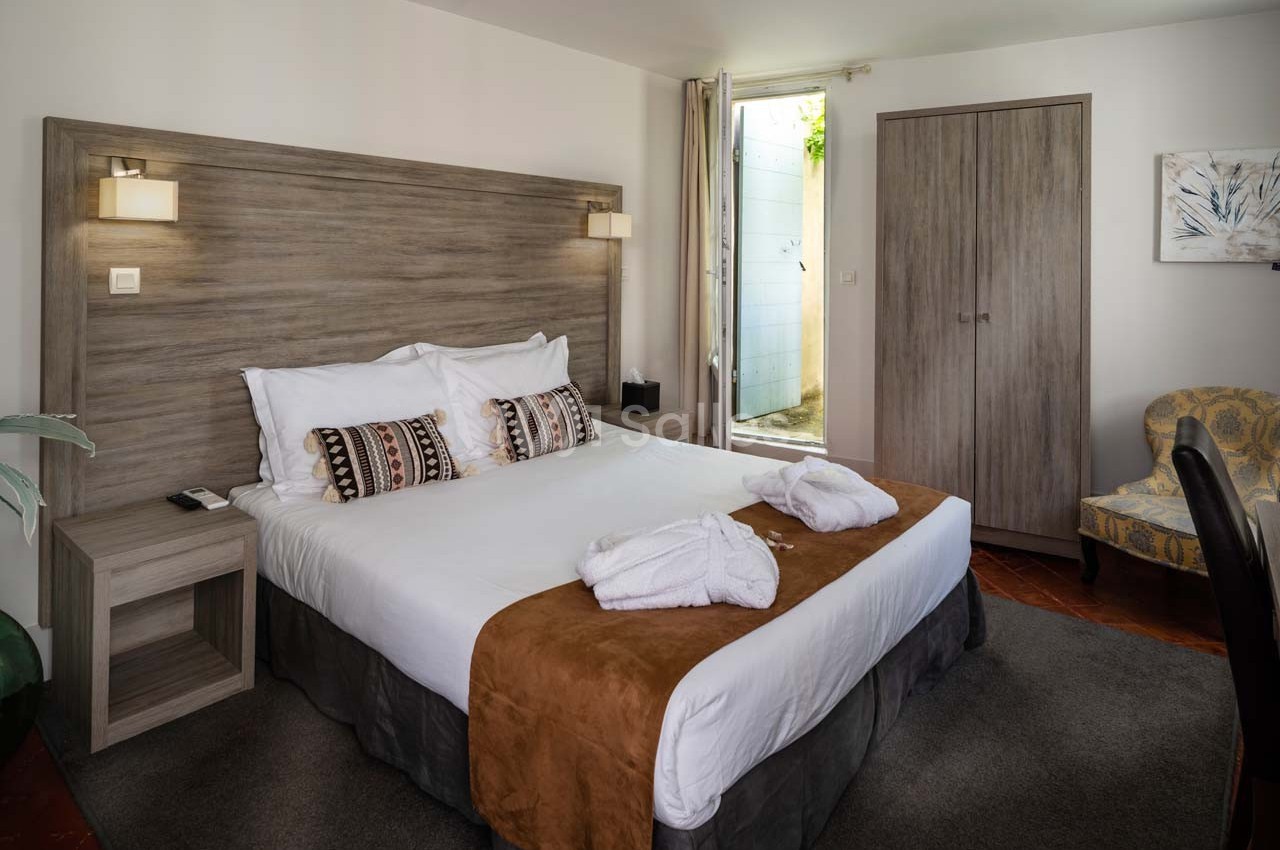 Chambre lumineuse avec lit double, tête de lit en bois, peignoirs posés, armoire et fauteuil dans un décor sobre.