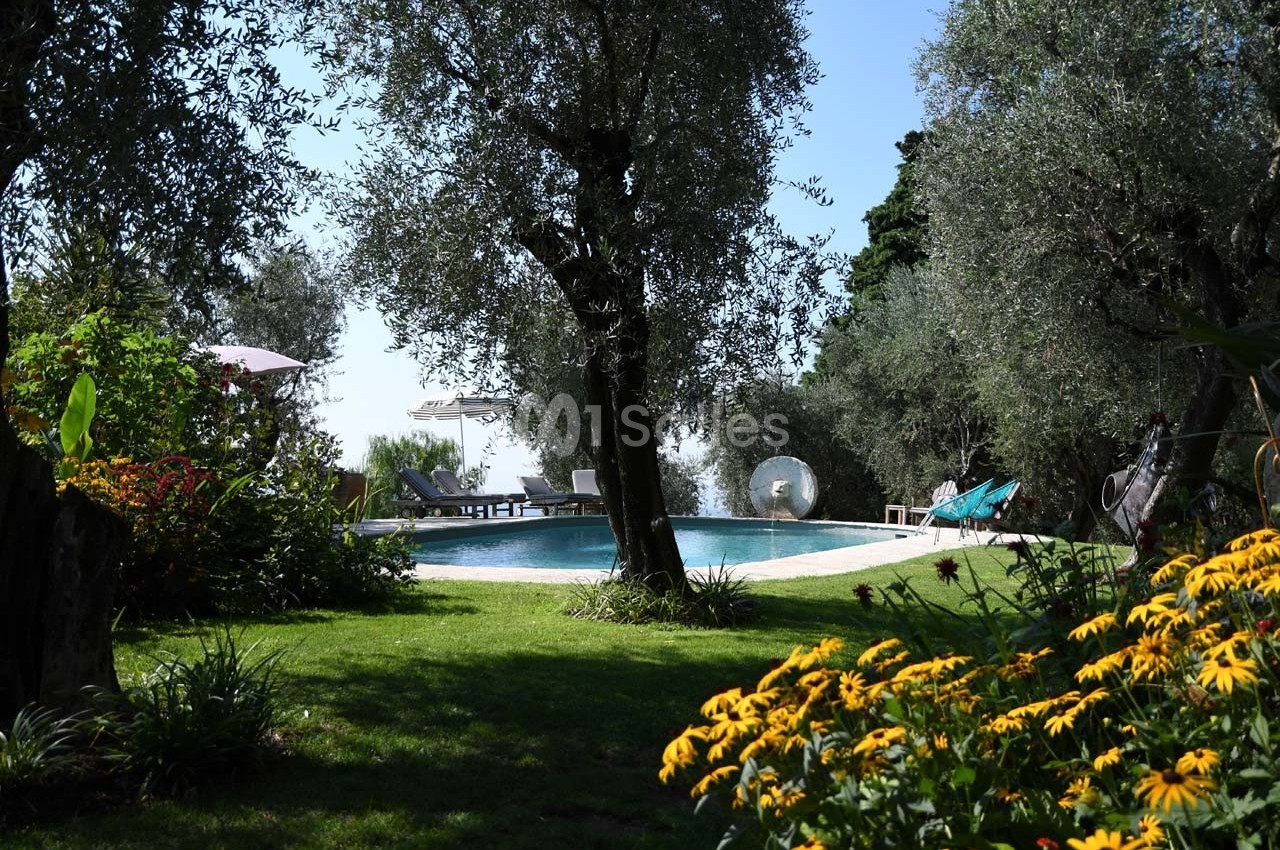 Jardin verdoyant avec des arbres et des fleurs entourant une piscine extérieure sous un ciel dégagé.