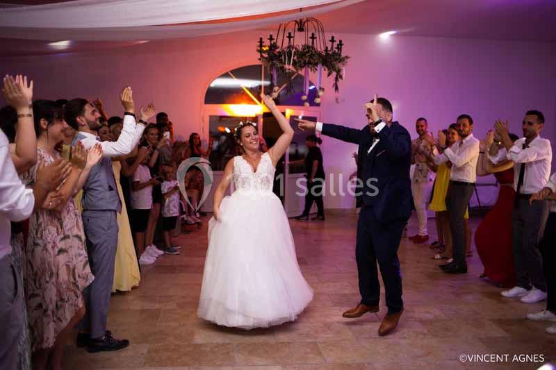 Un couple de mariés danse au centre d'une salle entouré d'invités applaudissant.