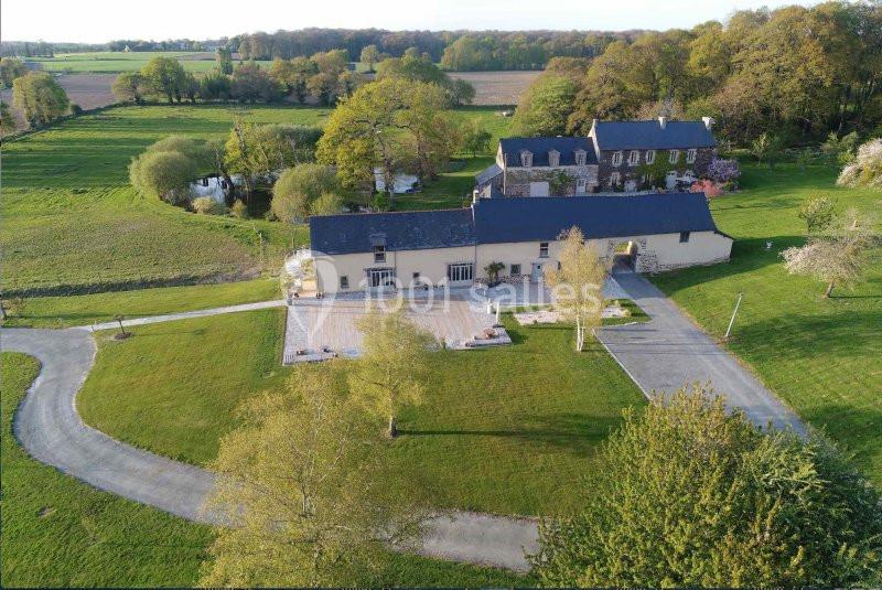 Vue aérienne d'un domaine rural avec bâtiments en pierre, terrasse, allée sinueuse et paysage verdoyant.