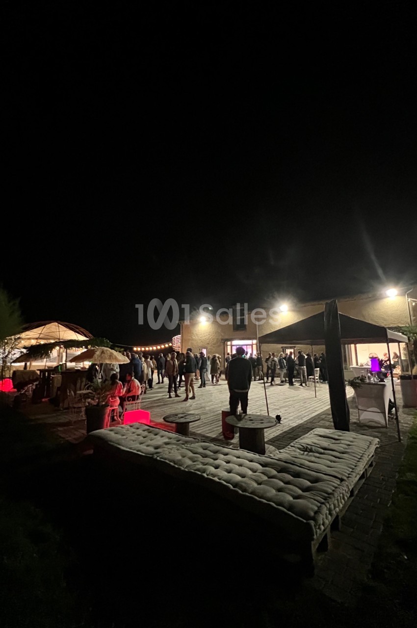 Groupe de personnes rassemblées de nuit sur une terrasse éclairée, avec des guirlandes lumineuses et des espaces aménagés.