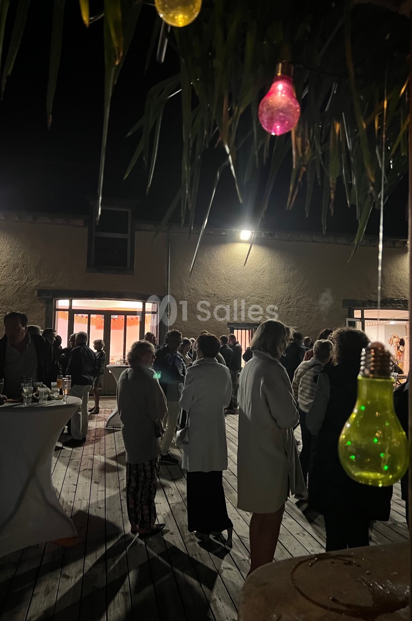 Groupe de personnes rassemblées en soirée sur une terrasse en bois, éclairée par des lumières suspendues.