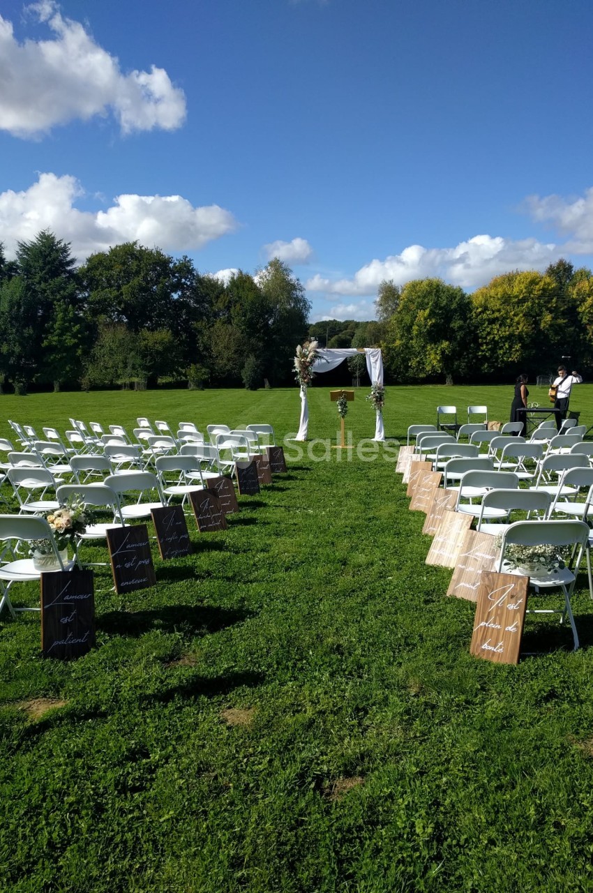 Chaises blanches disposées en rangées sur une pelouse pour une cérémonie en plein air, avec une arche décorée au centre.