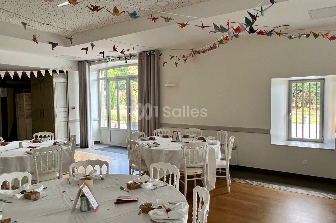 Salle de réception lumineuse décorée de guirlandes en origami, avec des tables rondes dressées pour un événement.