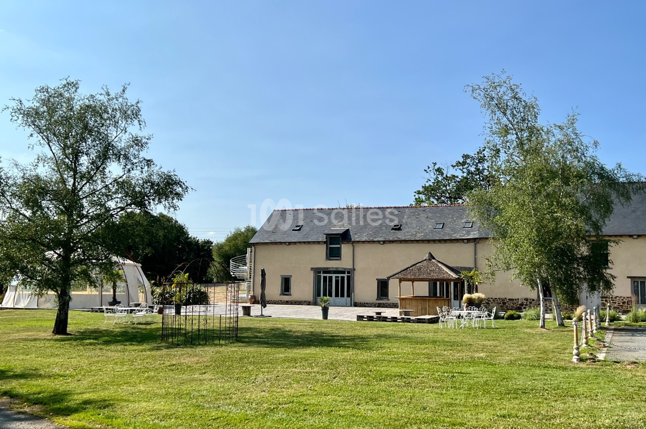 Bâtiment en pierre rénové avec toit en ardoise, entouré d'un jardin verdoyant et d'une terrasse aménagée.