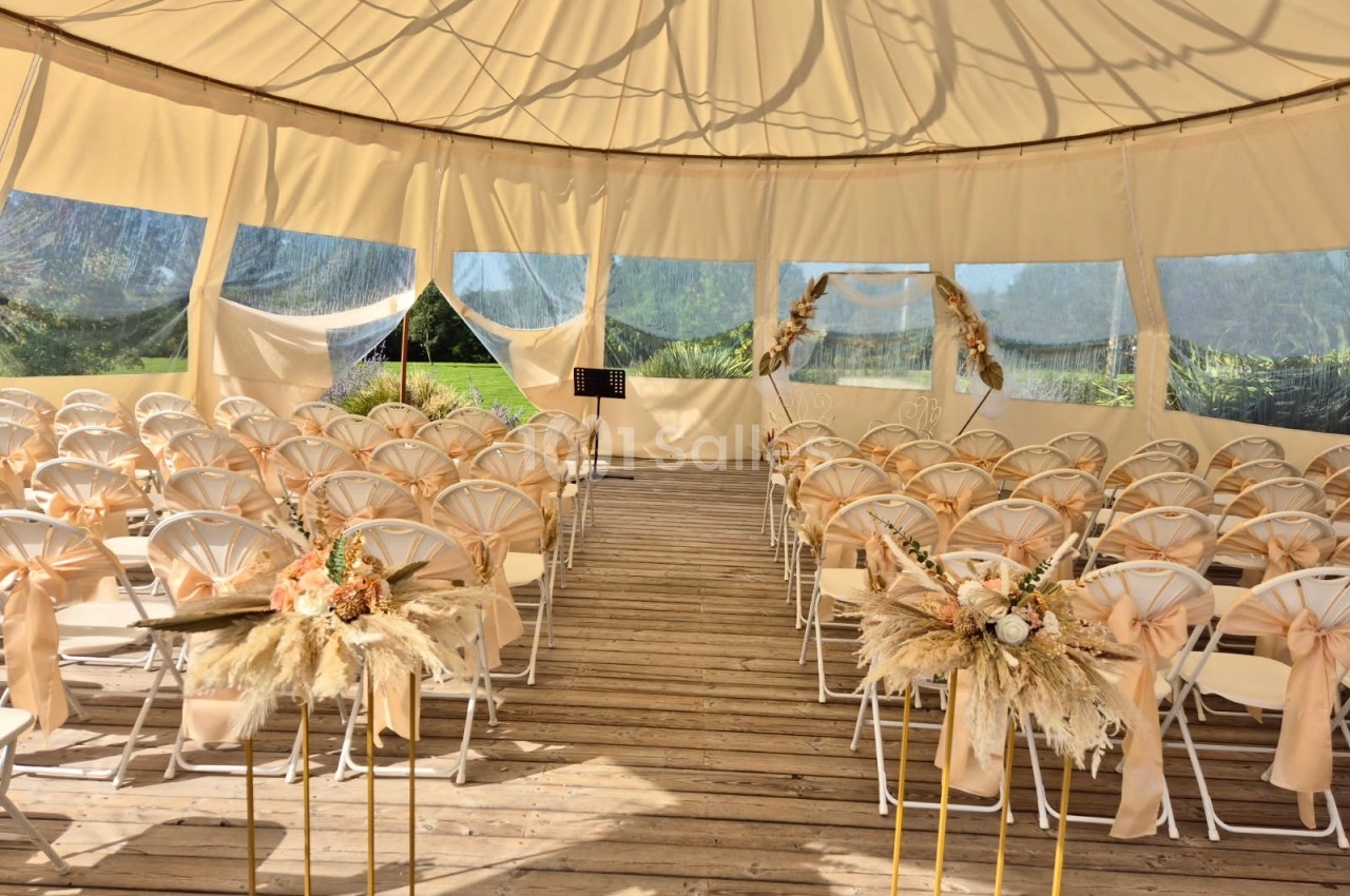 Salle de cérémonie en plein air sous une tente, avec des chaises décorées et des compositions florales.