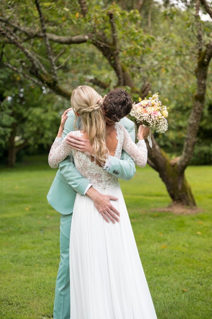 Un couple de mariés s'enlace dans un jardin, la mariée tenant un bouquet de fleurs pastel.