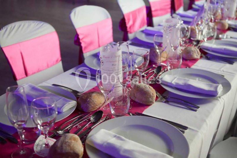 Table dressée pour un repas, avec nappes blanches, serviettes pliées, assiettes, couverts, verres et décorations roses.