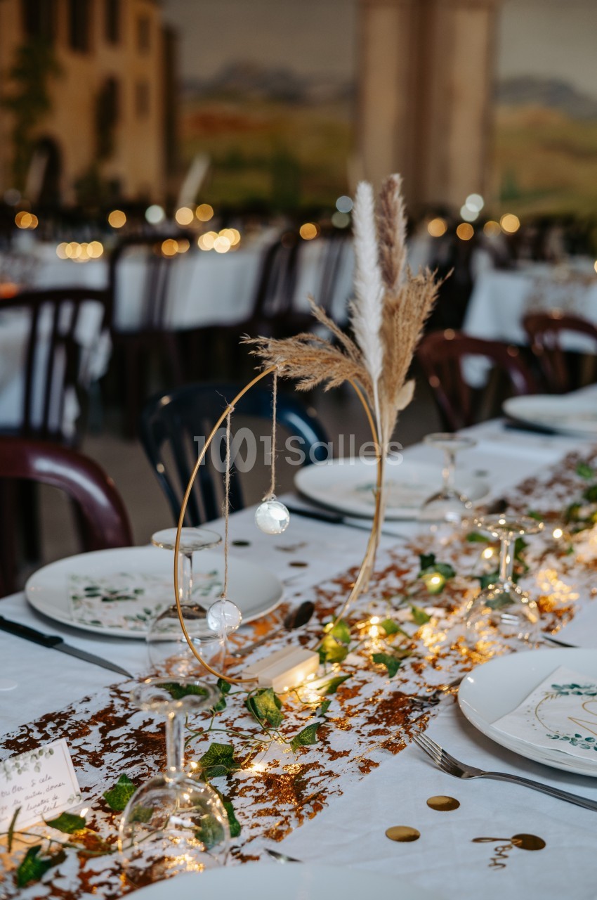 Centre de table décoratif avec pampas, guirlandes lumineuses et éléments naturels sur une nappe blanche.
