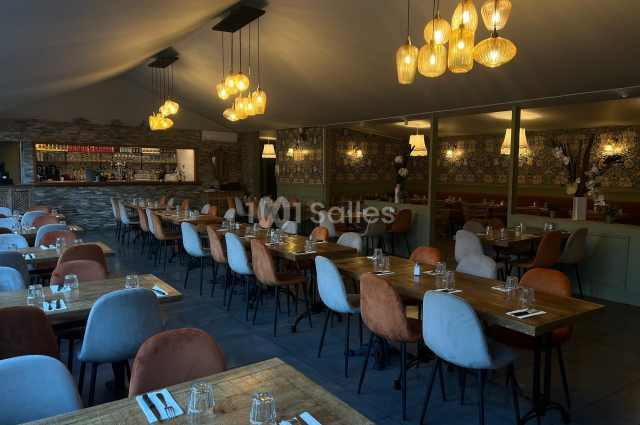 Salle de restaurant élégante avec tables en bois, chaises colorées et éclairage chaleureux suspendu.