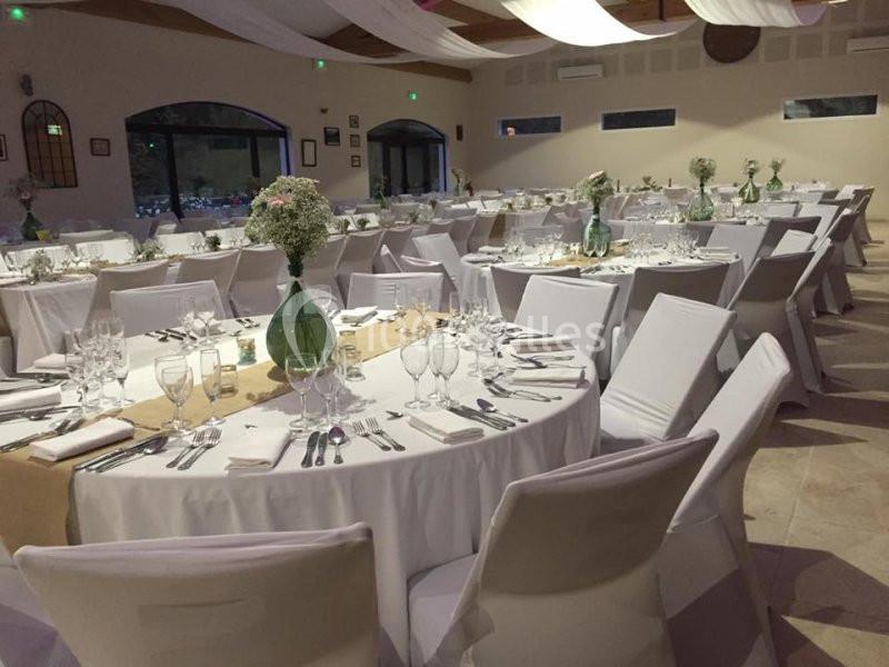Salle de réception décorée avec des tables rondes dressées, nappes blanches et centres de table fleuris.
