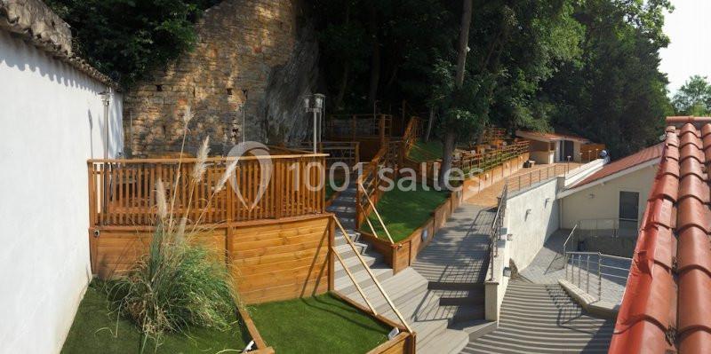 Terrasses en bois avec escaliers et espaces verts, adossées à une paroi rocheuse et entourées de végétation.