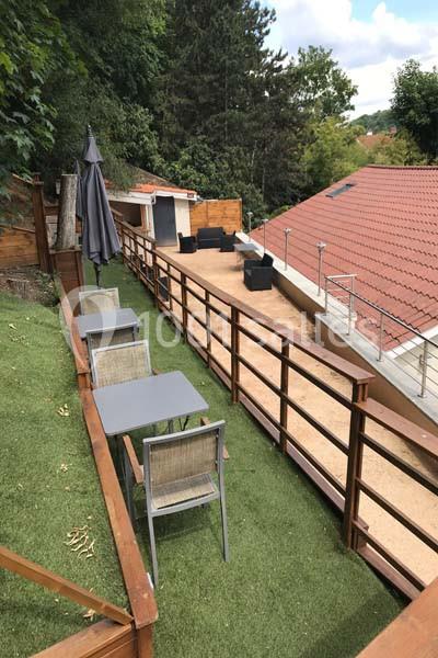 Terrasse en bois sur deux niveaux avec mobilier de jardin, pelouse artificielle et vue sur des toits voisins.