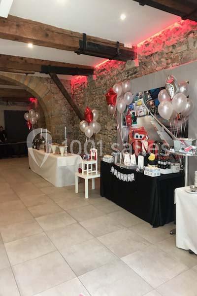 Salle décorée pour une fête avec ballons, tables garnies de cadeaux et murs en pierre apparente.