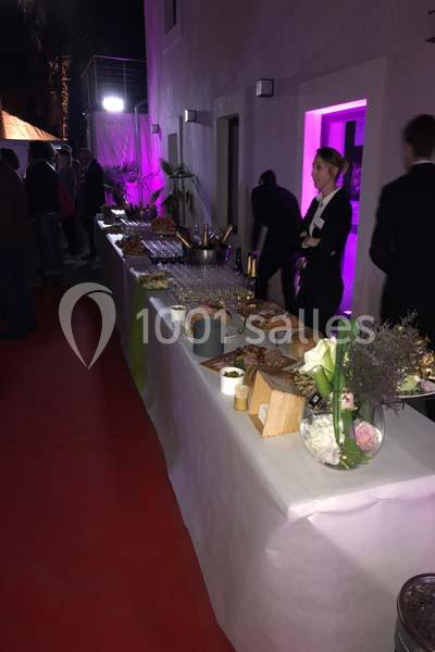 Buffet dressé avec plats variés, boissons et décorations florales, dans un espace éclairé par des lumières violettes.