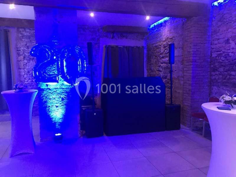 Salle décorée pour un événement avec des ballons ’20’, éclairage bleu, tables hautes et espace DJ.