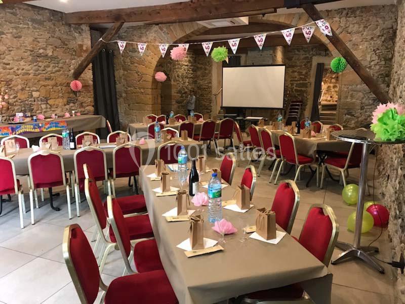 Salle décorée pour une réception avec tables dressées, chaises rouges, guirlandes et projecteur en arrière-plan.