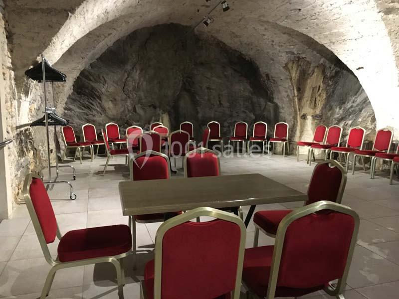 Salle voûtée en pierre avec des chaises rouges disposées autour d'une table centrale et sur les côtés.
