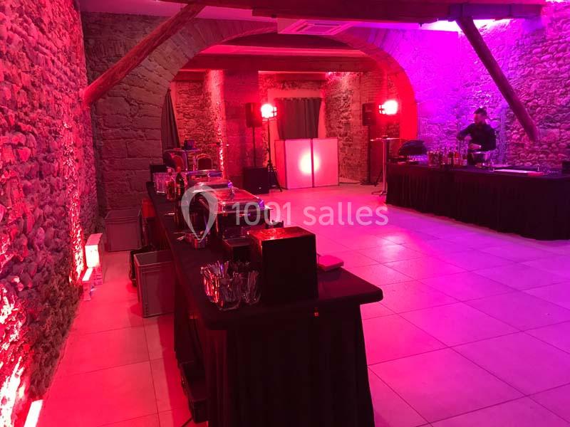 Salle en pierre éclairée par des lumières rouges et violettes, avec buffets installés et un bar en arrière-plan.
