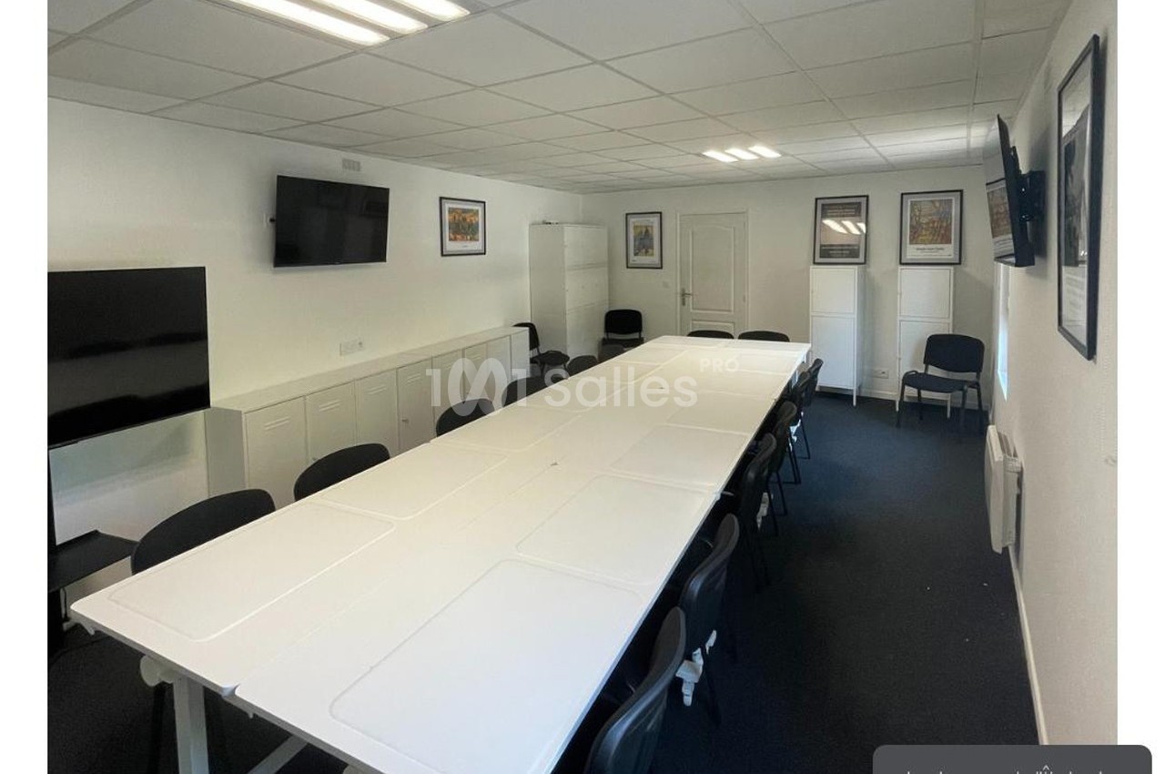 Salle de réunion lumineuse avec une grande table rectangulaire, des chaises noires et des écrans muraux.