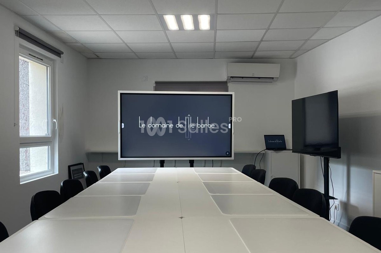 Salle de réunion lumineuse avec une grande table blanche, un écran interactif affichant ’Le domaine de l'île barbe’ et un…