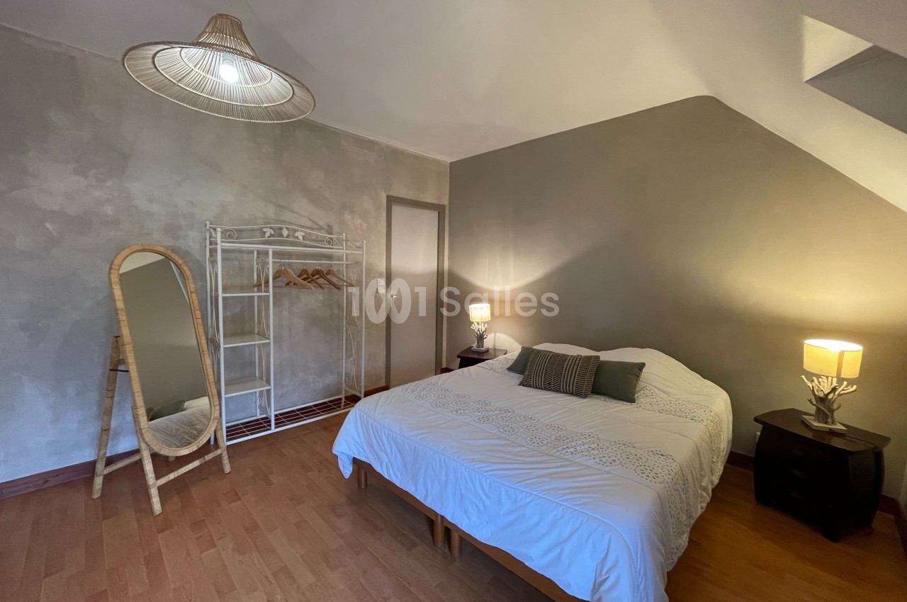 Chambre lumineuse avec lit double, miroir sur pied, étagère en métal et lampes de chevet sur tables noires.