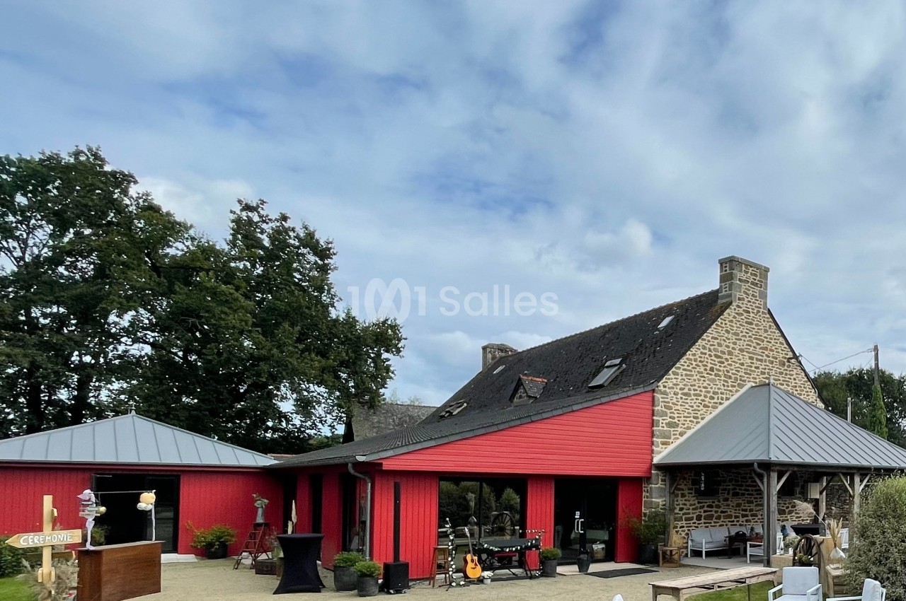 Bâtiment en pierre avec extensions rouges, entouré de mobilier extérieur blanc et d'arbres sous un ciel nuageux.