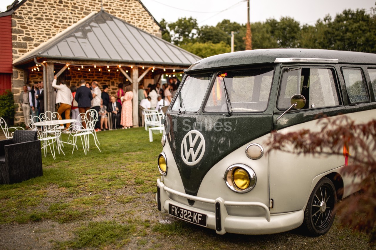 Un van Volkswagen vintage garé devant une réception en plein air près d'un bâtiment en pierre.