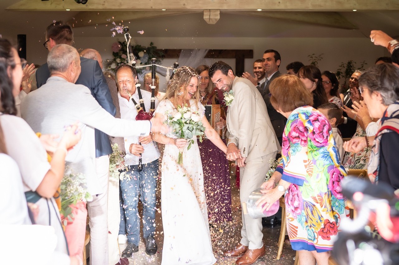 Un couple de mariés souriants sort sous une pluie de confettis, entouré d'invités applaudissant dans une salle festive.