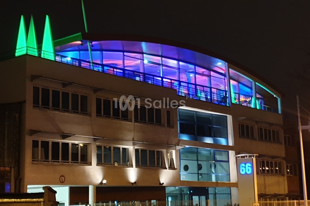 Bâtiment moderne éclairé de nuit avec des lumières colorées et un numéro 66 visible sur la façade.