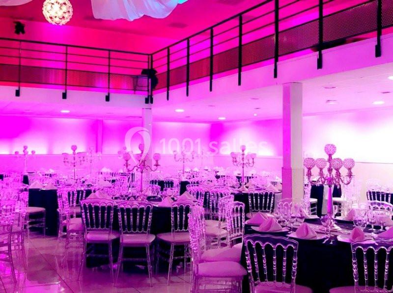 Salle de réception décorée avec des tables rondes, chaises transparentes et éclairage rose.