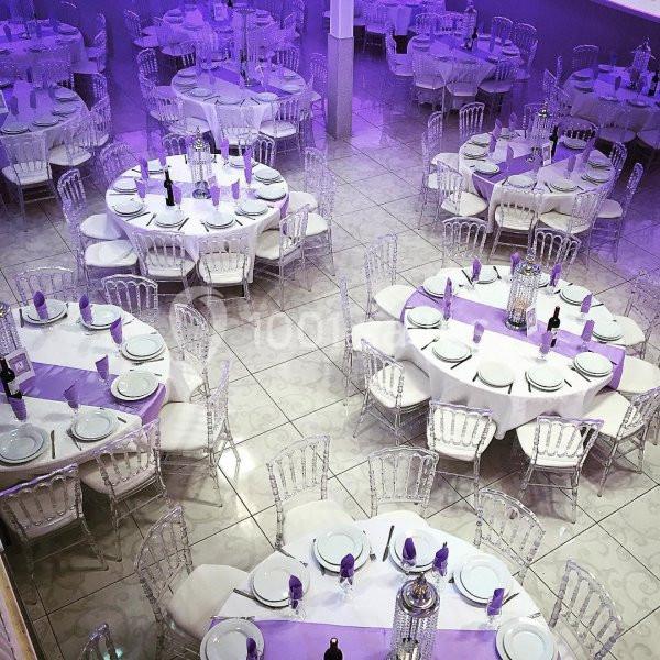 Salle de réception décorée avec des tables rondes dressées de nappes blanches et violettes, entourées de chaises…